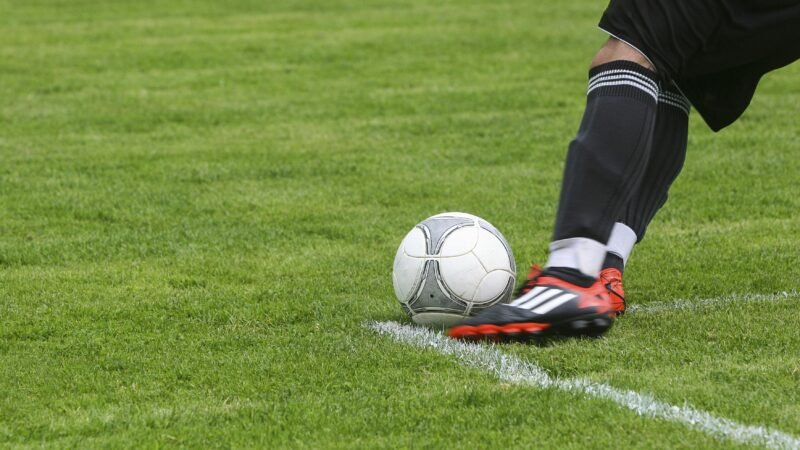Dynamic shot of a soccer player kicking the ball on a grassy field, showcasing fast-paced sports action.