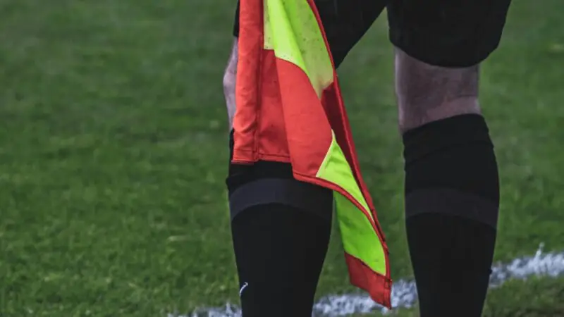 A soccer referee stands with a flag on the grass field during a match.