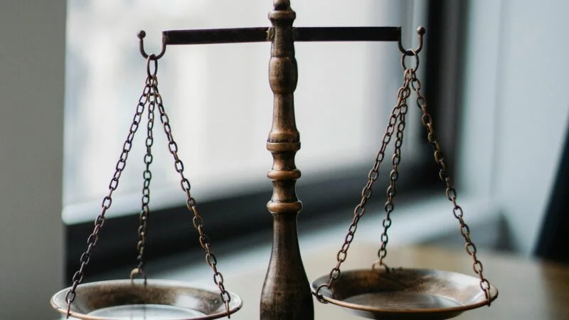Decorative judgement scale and gavel placed on desk in light lawyer office against window