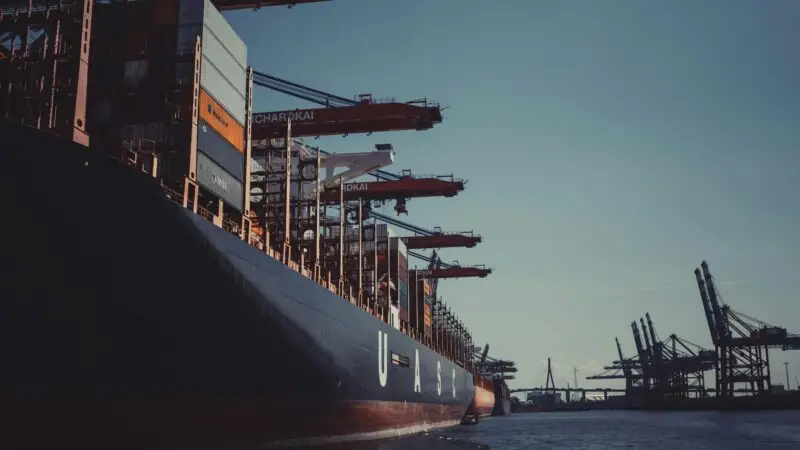 A large cargo ship docked at Hamburg Harbor, cranes loading containers under a clear sky.