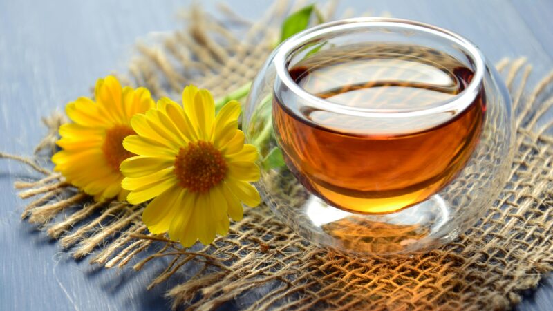 Glass cup of herbal tea with yellow flowers on a textured background.