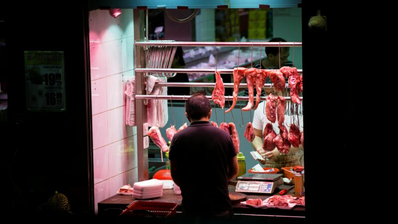 Butcher working in a vibrant Hong Kong market stall preparing fresh cuts of meat.