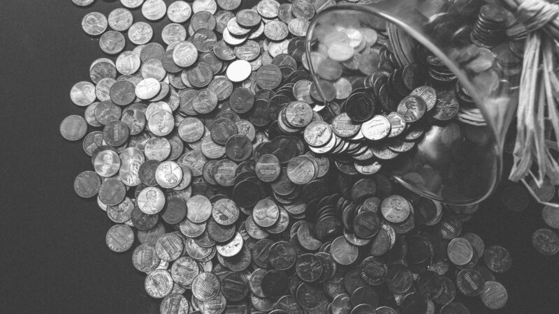 Monochrome image of coins spilling from a glass jar, symbolizing wealth and savings.