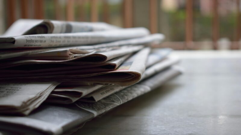 A close-up of a stack of newspapers resting on a desk, symbolizing information and media.