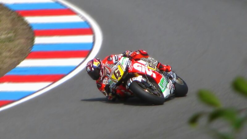 Motorcycle racer leans into a sharp curve on a high-speed track during a competition.
