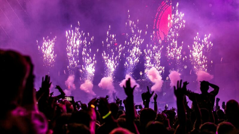 Vibrant EDM concert scene with fireworks, smoke, and enthusiastic crowd enjoying the music.