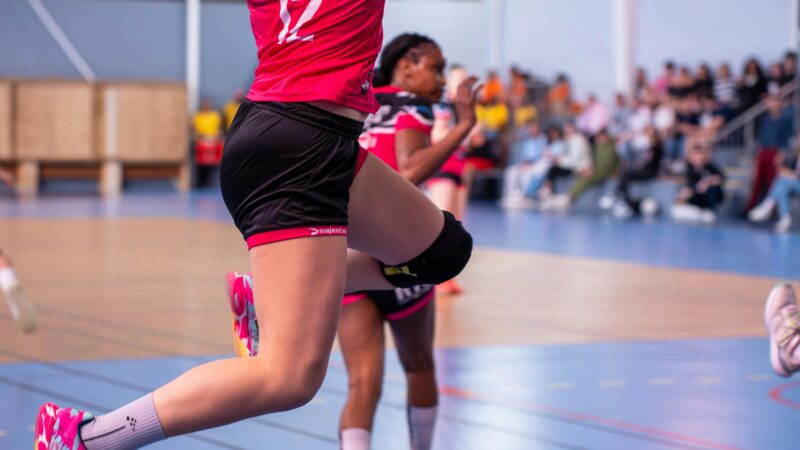 Female handball player jumping in mid-air during an intense match indoors.
