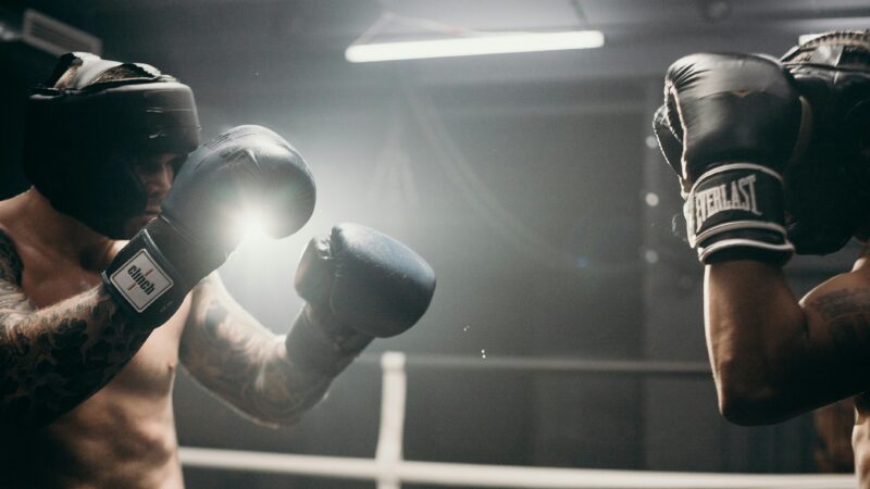 Two men sparring in a dimly lit gym, showcasing intense boxing training and athleticism.